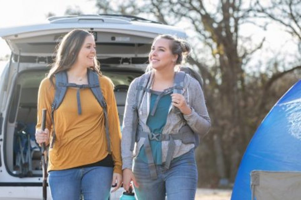 Women smile while embarking on hike after parking car at campsite