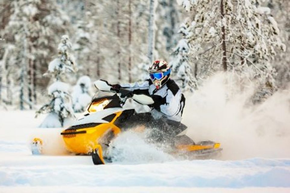 The rider in gear with a helmet drifting on a snowmobile on a deep snow surface on a background of snowy landscaping nature and winter forest.