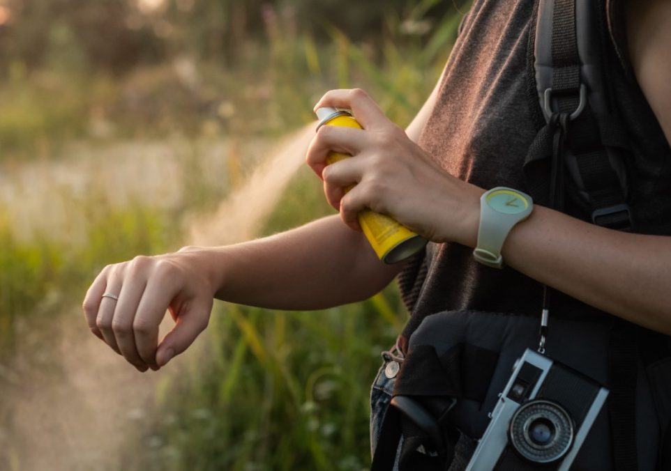 A woman hiking sprays bug spray on her arm to protect herself from insects.