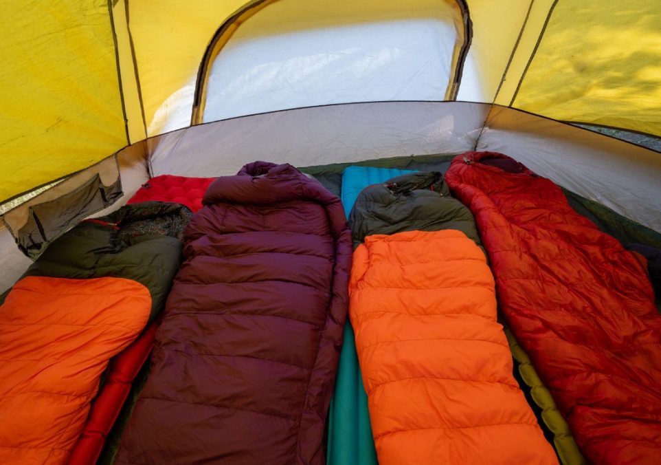 Four colorful sleeping bags in a row, each resting on a camping sleeping pad, showcasing vibrant outdoor gear.